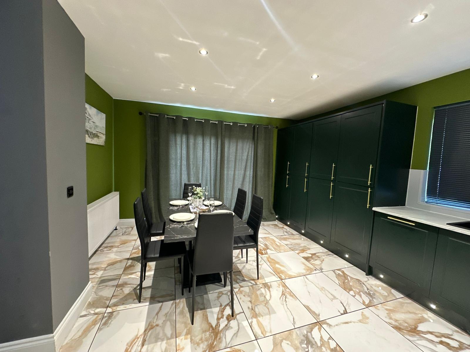 Kitchen and dining room with dark green cabinets, a set dining table and marble-effect floor tiles