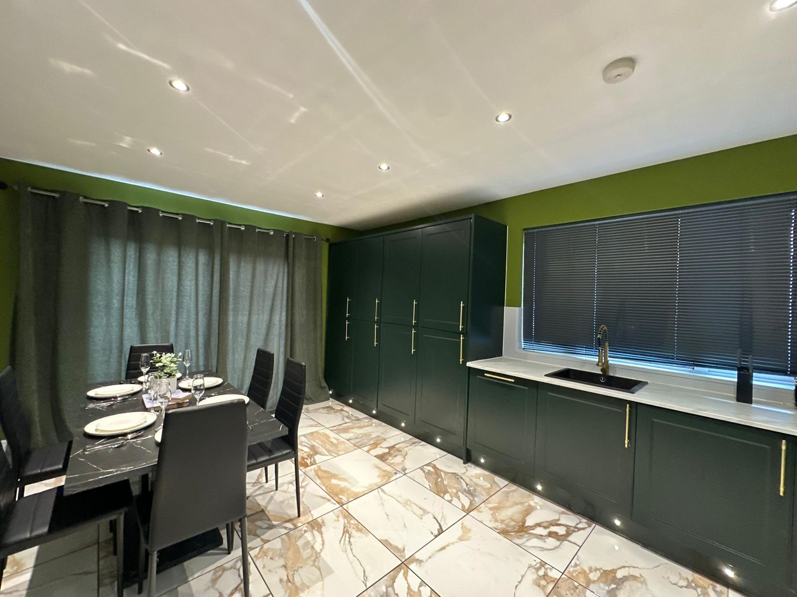 Dark green fitted kitchen with a sink, dining table and marble-effect floor tiles